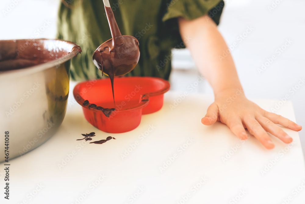 The child pours chocolate dough into a red silicone mold on a white table. Making a Christmas cookie. The child pours chocolate dough into a red silicone mold on a white table. Making a Christmas cookie.