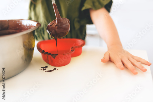 The child pours chocolate dough into a red silicone mold on a white table. Making a Christmas cookie.