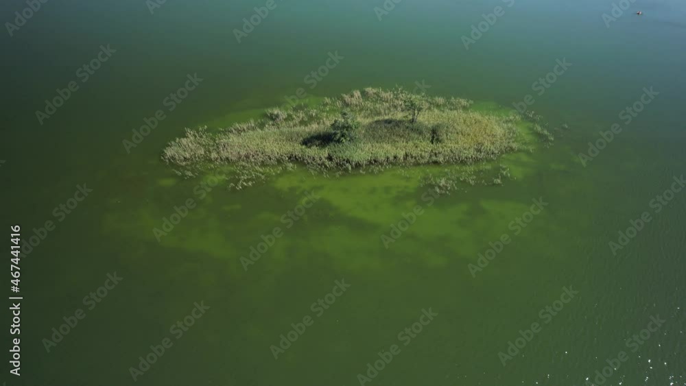 Aerial view of the small island in the middle of a shallow lake. Slow drone flight over water, zoom in. Sun's rays on the water. Aerial view of the small island in the middle of a shallow lake. Slow drone flight over water, zoom in. Sun's rays on the water.