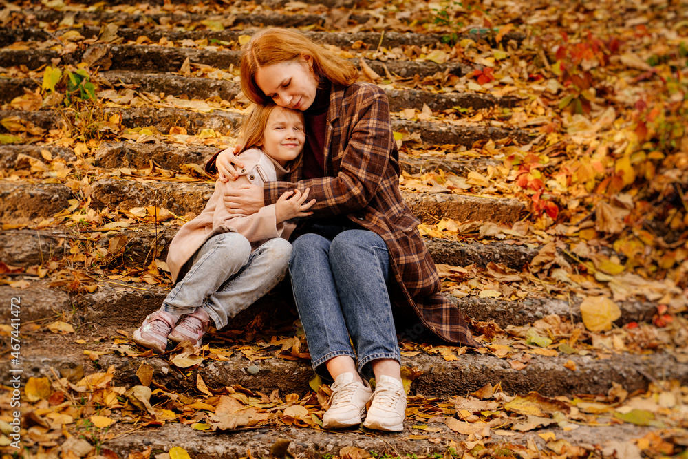 mother and daughter sit and hug on the stairs in the autumn park. mother and daughter sit and hug on the stairs in the autumn park.
