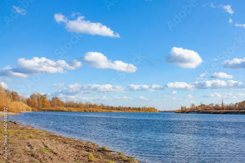 Beautiful clouds in the blue sky. Autumn landscape on a bright sunny day. Yellow forest on the bank of the blue river.