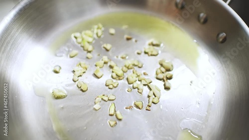 Macro closeup of sizzling sliced cut pieces of fresh garlic fried on stainless steel frying pan with olive oil at home kitchen cooking