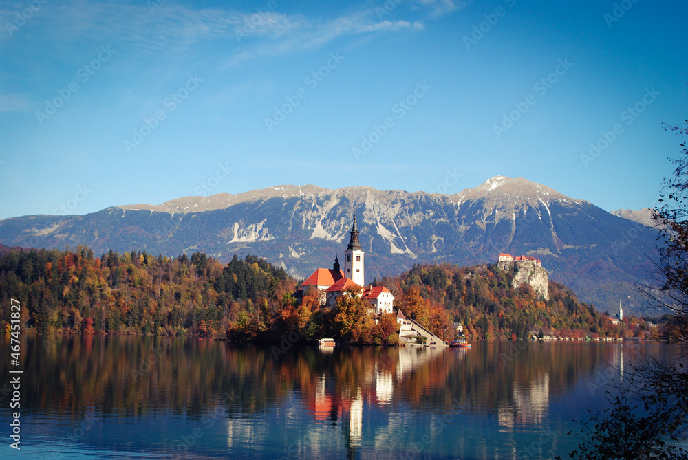 Famous alpine Bled lake in Slovenia, amazing autumn landscape. Scenic view of the lake, island with church, Bled castle, mountains and blue sky Famous alpine Bled lake in Slovenia, amazing autumn landscape. Scenic view of the lake, island with church, Bled castle, mountains and blue sky