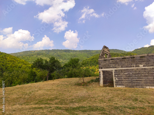 Village in the dry season with a view of green trees on the hill, the sky full of clouds and an old ruined house