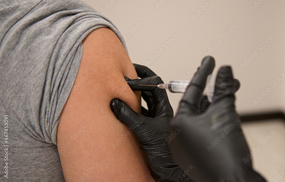 Close-up. Hands of doctor in protective medical gloves, injecting a vaccine to volunteer. Unrecognizable patient vaccinated against corona virus or viral infectious diseases. Clinical research, trial