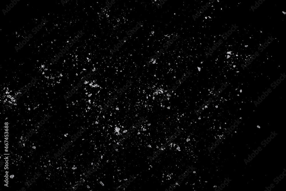 White crystals of sugar scattered on a black surface.