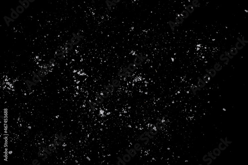 White crystals of sugar scattered on a black surface.