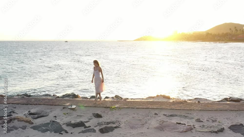Young beautiful girl ballerina is dancing on the beach near the sea on the golden sunset. ballerina is dancing along the path by the sea, drone follows her. back sunset light Young beautiful girl ballerina is dancing on the beach near the sea on the golden sunset. ballerina is dancing along the path by the sea, drone follows her. back sunset light
