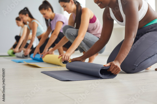 Crop of diverse women roll mats training working out together at group class in fitness club. Smiling multiracial girls prepare for yoga meditation practice. Sport, healthy lifestyle concept.
