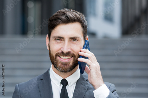 Close-up portrait photo of successful bearded businessman smiling talking on the phone