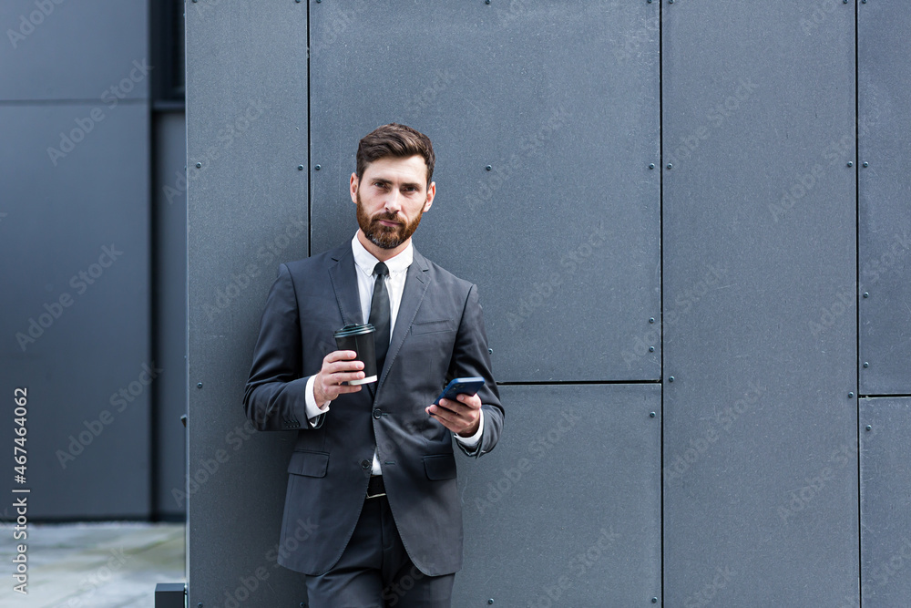Bearded businessman in formal suit on break using mobile phone use  smartphone. business man standing outside on modern urban city street  background with coffee cup in downtown outdoors. copy space Stock Photo