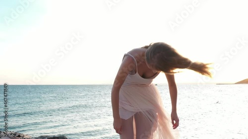 Young beautiful girl ballerina is dancing on the beach near the sea on the golden sunset. Moving woman, charming actress smile. Drone flies near dancer by ocean. ballerina dresses, straightens dress