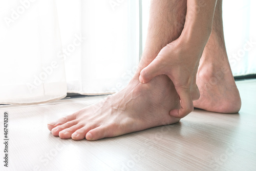 Ankle Pain man sitting on wooden background holding her feet. Health concept. © Photo Sesaon