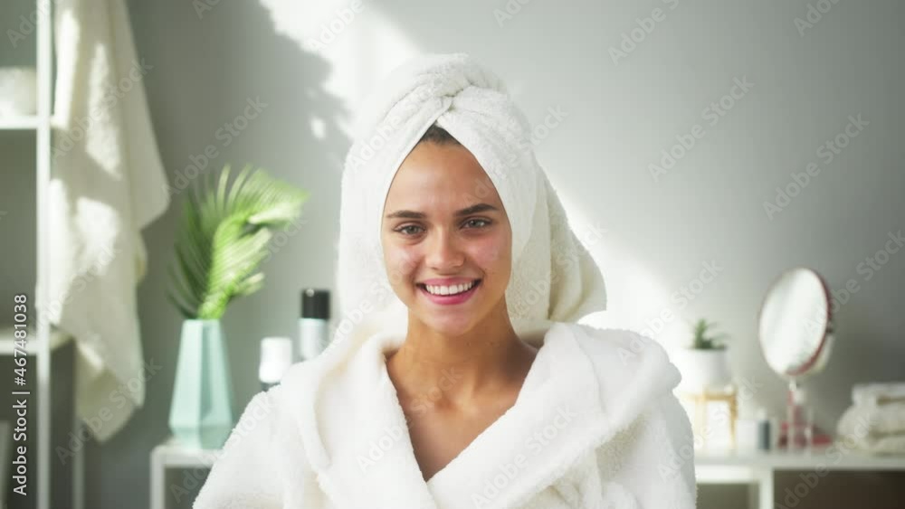 Happy woman smiling in bathroom or spa salon. Portrait of young female student wearing white bathrobe and towel on head after shower. Natural day make up, facial skin care concept. Happy woman smiling in bathroom or spa salon. Portrait of young female student wearing white bathrobe and towel on head after shower. Natural day make up, facial skin care concept.