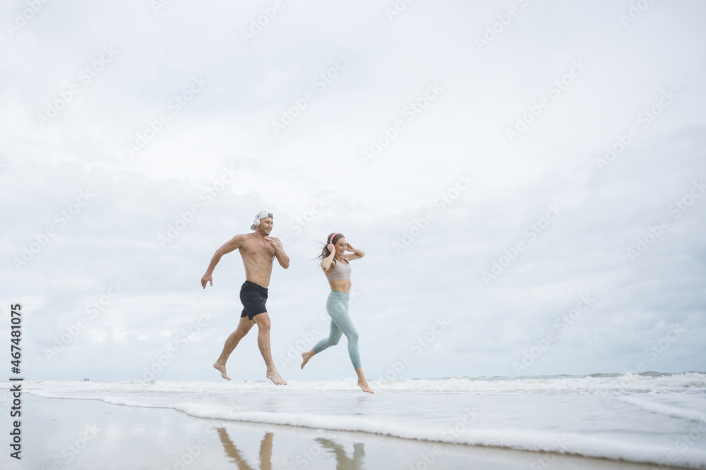 Runners. Young couple running on beach. Sport runners jogging on beach working out smiling happy. Fitness exercise concept Runners. Young couple running on beach. Sport runners jogging on beach working out smiling happy. Fitness exercise concept