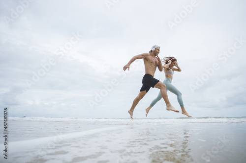 Runners. Young couple running on beach. Sport runners jogging on beach working out smiling happy. Fitness exercise concept
