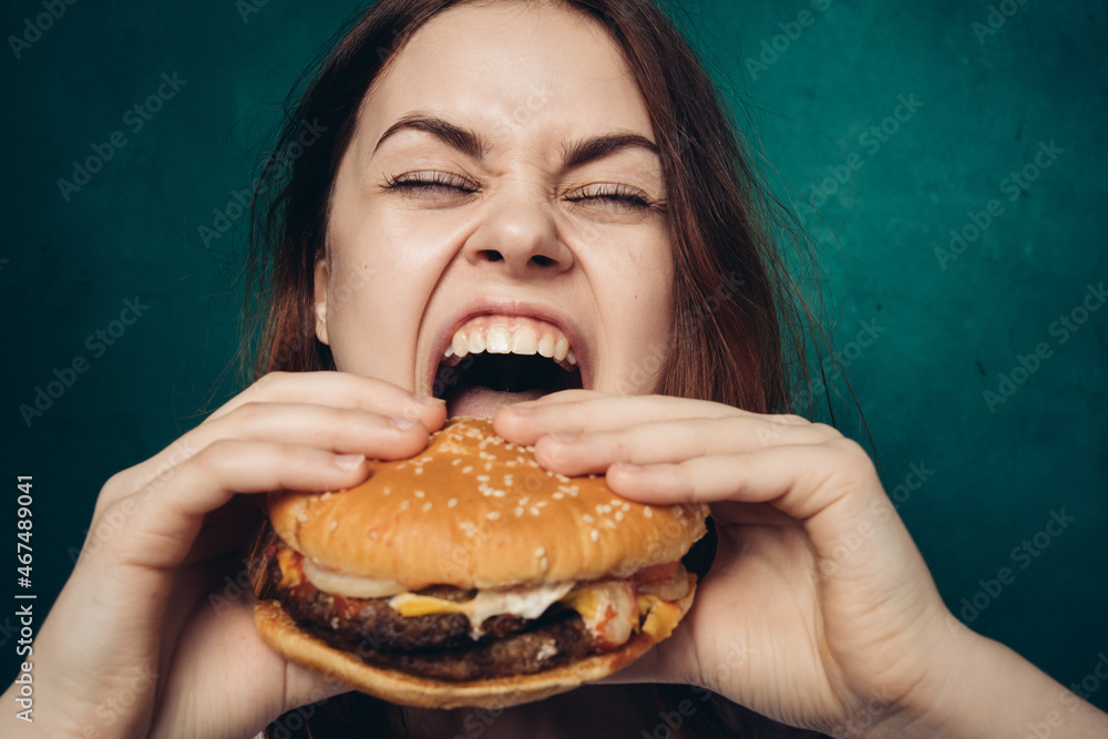 cheerful woman with hamburger near face snacking fast food