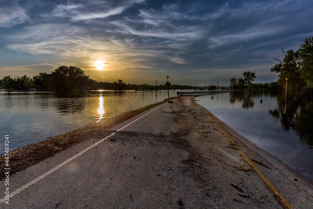 Sunset Over Flooded Roadway. Beautiful sunset reflecting over flooded road with gray clouds and trees reflecting in river. Copy Space.