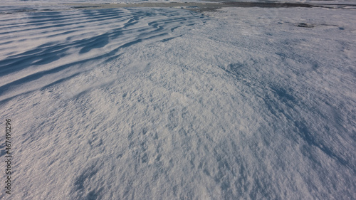 Snow on a frozen lake. Full screen. Close-up. A smooth surface, and in the upper left corner - snow dunes form a pattern. A patch of ice is visible in the distance. Baikal