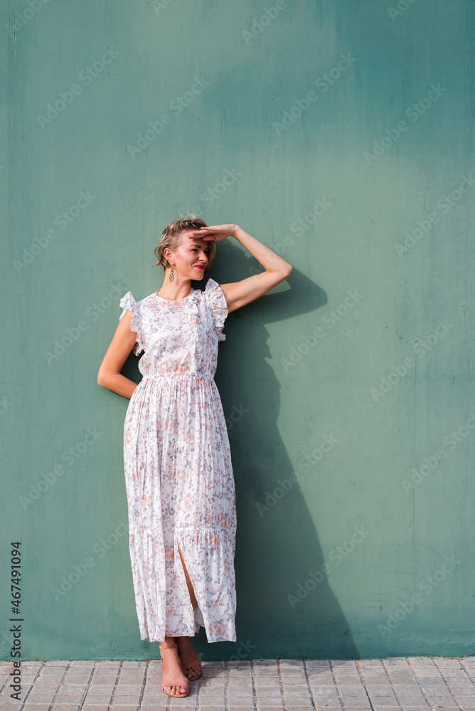 vertical portrait of an attractive blonde woman on floral dress. She is protecting her eyes from sun with her hands vertical portrait of an attractive blonde woman on floral dress. She is protecting her eyes from sun with her hands