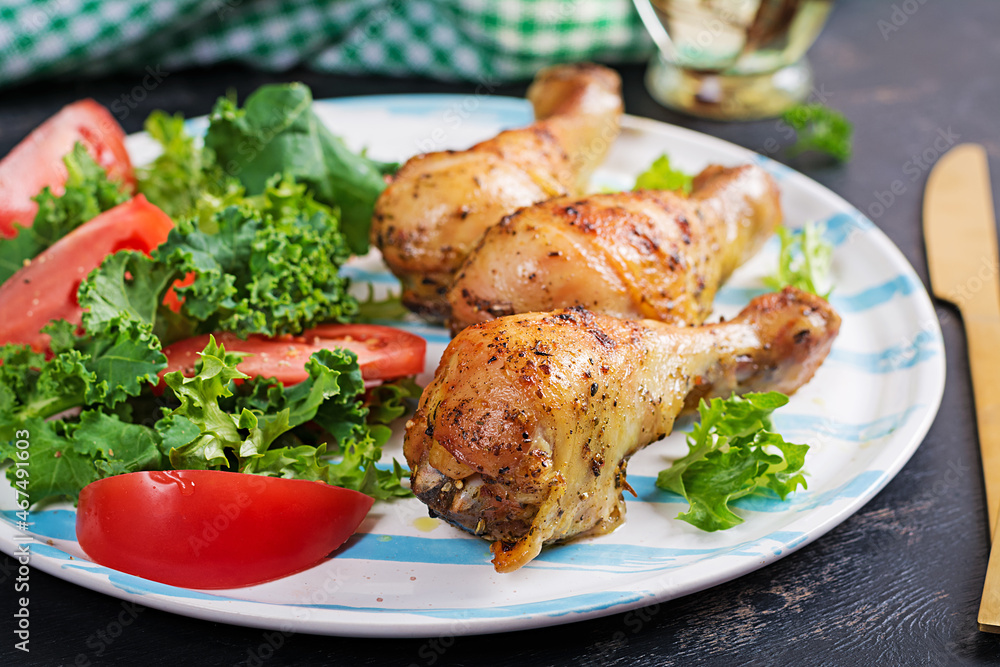 Baked chicken drumsticks and fresh salad on a dark background. Baked chicken drumsticks and fresh salad on a dark background.