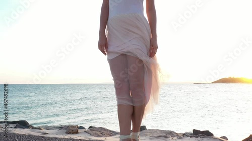 Young beautiful girl ballerina is dancing on the beach near the sea on the golden sunset. Moving woman, charming actress smile. Drone flies near dancer on the ocean shore. 