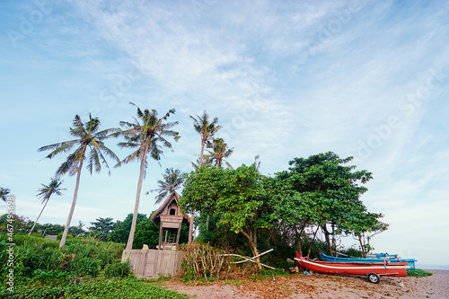 Beautiful landscape with bungalow and fishing boats under palm trees on the beach.