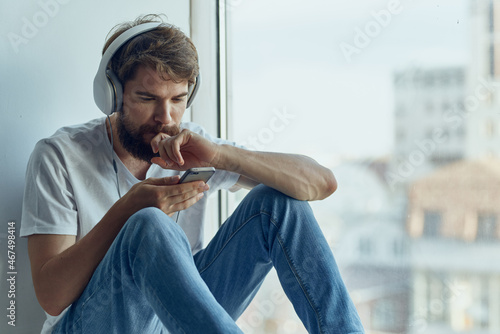 man in white t-shirt sitting on the windowsill in headphones in headphones