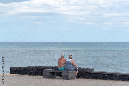 un pareja de personas mayores de espaldas sentado en un banco mirando el mar cerca de la playa. 