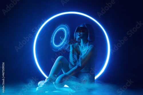Woman with futuristic tablet in hand. Girl in glasses of virtual reality presses start button. Augmented reality, future technology, AI concept. Holographic interface to display data. Dark background.