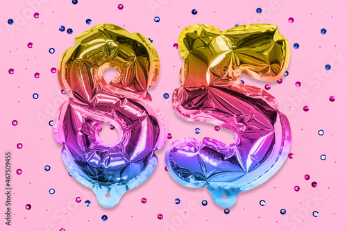 Rainbow foil balloon number, digit eighty five on a pink background with sequins. Birthday greeting card with inscription 85. Anniversary concept. Numerical digit. Celebration event, template. © Marina Kaiser