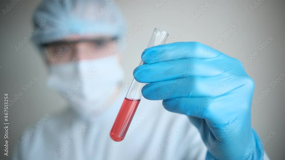 An epidemiologist in a white coat and blue gloves demonstrates a test tube for collecting analysis with a red reagent. Development of a drug against the virus. Selective focus An epidemiologist in a white coat and blue gloves demonstrates a test tube for collecting analysis with a red reagent. Development of a drug against the virus. Selective focus