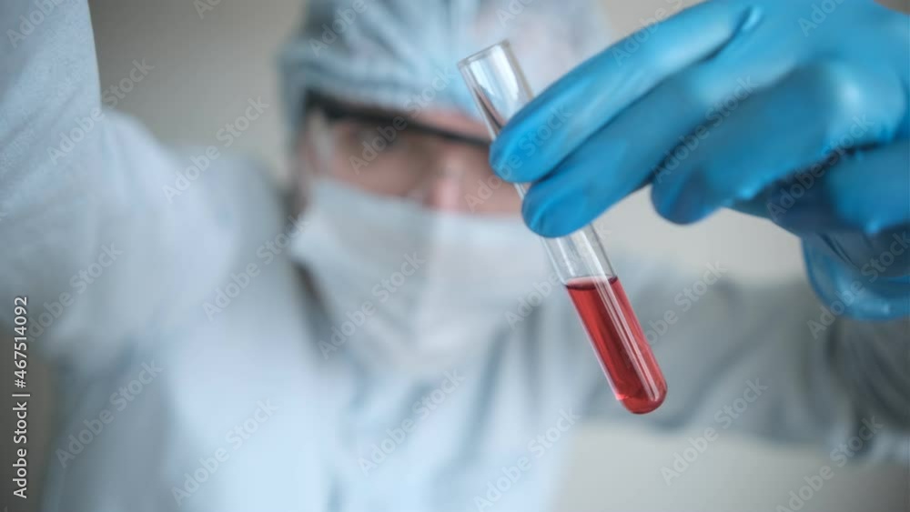 An epidemiologist in a white coat and blue gloves demonstrates a test tube for collecting analysis with a red reagent. Development of a drug against the virus. Selective focus An epidemiologist in a white coat and blue gloves demonstrates a test tube for collecting analysis with a red reagent. Development of a drug against the virus. Selective focus