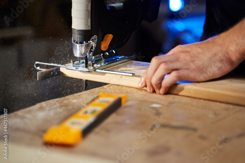 men's hands sawing a piece of wood with a jigsaw