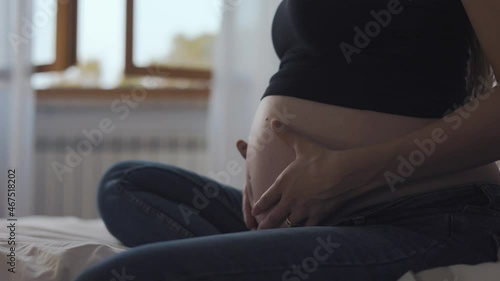 4K footage of a pregnant girl lying on the bed touches her baby bump