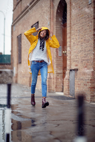A young handsome woman in a yellow raincoat is enjoying rain drops while walking the city on a rainy day. Walk, rain, city