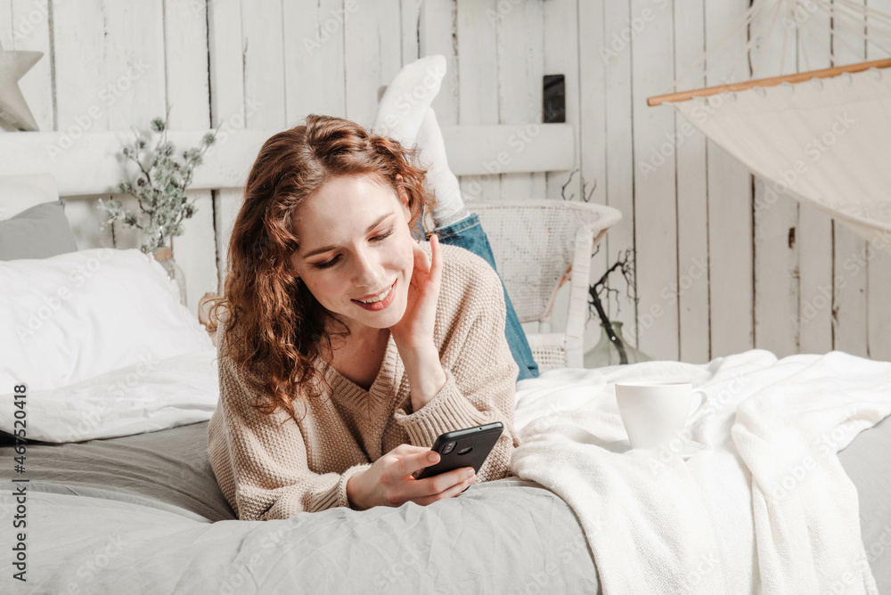 Φωτογραφία Beautiful caucasian girl lyes on the bed and looks in the phone smiling christma