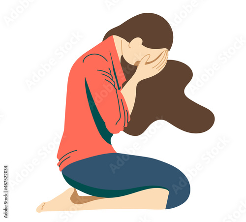 Young girl, a teenager suffering from psychological illnesses, depression, anxiety, is sitting on the floor with her face covered with her hands and her head lowered