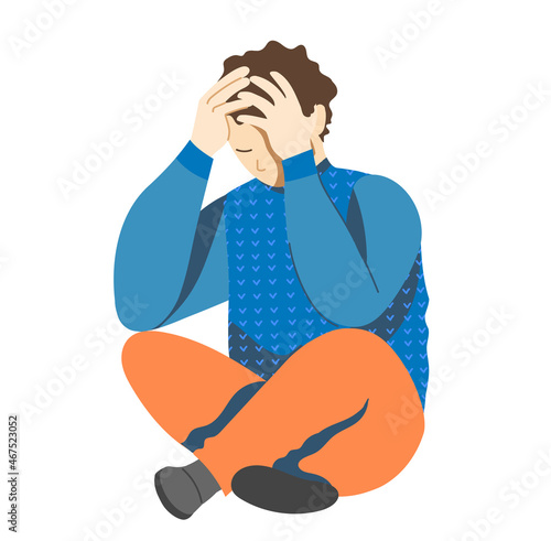 Young man, teenager suffering from psychological illnesses, depression, anxiety, sits sadly on the floor, holding his head in his hands