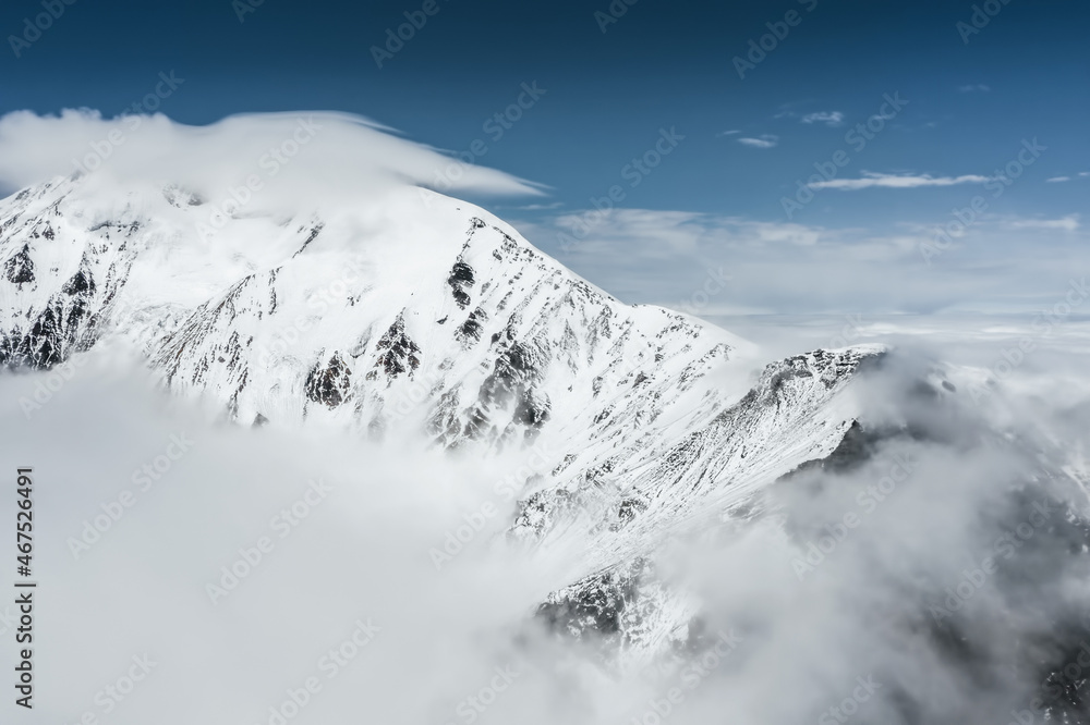 Crater of the Tolbachik volcano, snowy peak of summit and crater in the clouds. Drone aerial view Crater of the Tolbachik volcano, snowy peak of summit and crater in the clouds. Drone aerial view