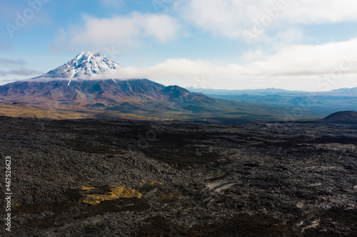 Black frozen lava flow from crater on the slopes of Tolbachik volcanoes, on background Bolshaya Udina volcano, Kamchatka, Russia