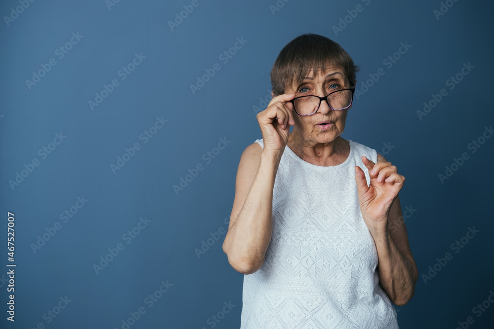 Portrait of elderly woman on gray-blue background carefully looking at the camera through glasses Portrait of elderly woman on gray-blue background carefully looking at the camera through glasses