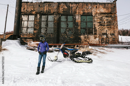 Female rider with snowbike in abandoned winter frozen village. Old fashion russian stile houses in Priiskovoe Russia photo