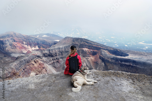 Woman with dog and backpack sitting  on the mountain top above crater and lake of Gorely volcano, Kamchatka photo