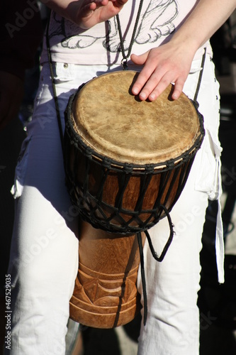 Hands are tapping on an African drum. A sunny summer day. Fingers and nails. A brown drum in a mesh. Warm and sunny