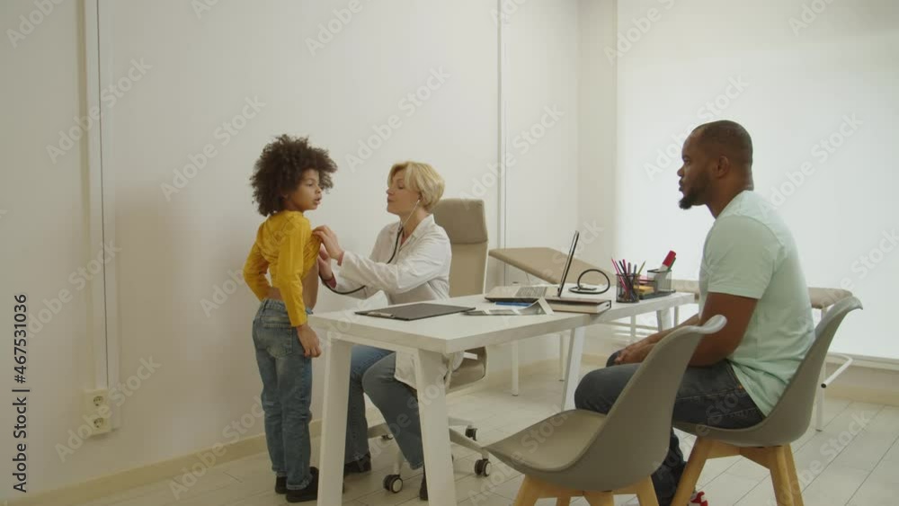 Caring pretty professional middle aged woman physician examining, auscultating sick adorable preschool age african american boy with stethoscope while family visiting pediatrician in medical clinic Caring pretty professional middle aged woman physician examining, auscultating sick adorable preschool age african american boy with stethoscope while family visiting pediatrician in medical clinic