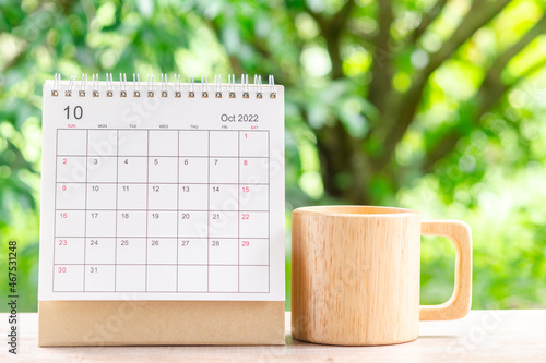 October month, Calendar desk 2022 for organizer to planning and wooden coffee cup on wooden table with green nature background. photo