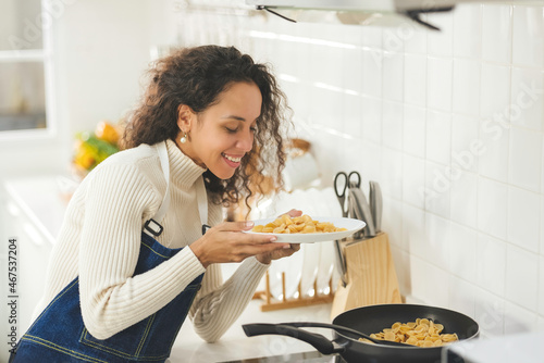 Beautiful young black woman is smiling and cooking in the bright white kitchen. wife or housewife is preparing to cook healthy food for the family. Stay at home. Recive order for food delivery. photo