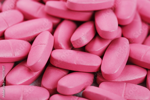 Pink pills with multivitamins in full screen as a background.