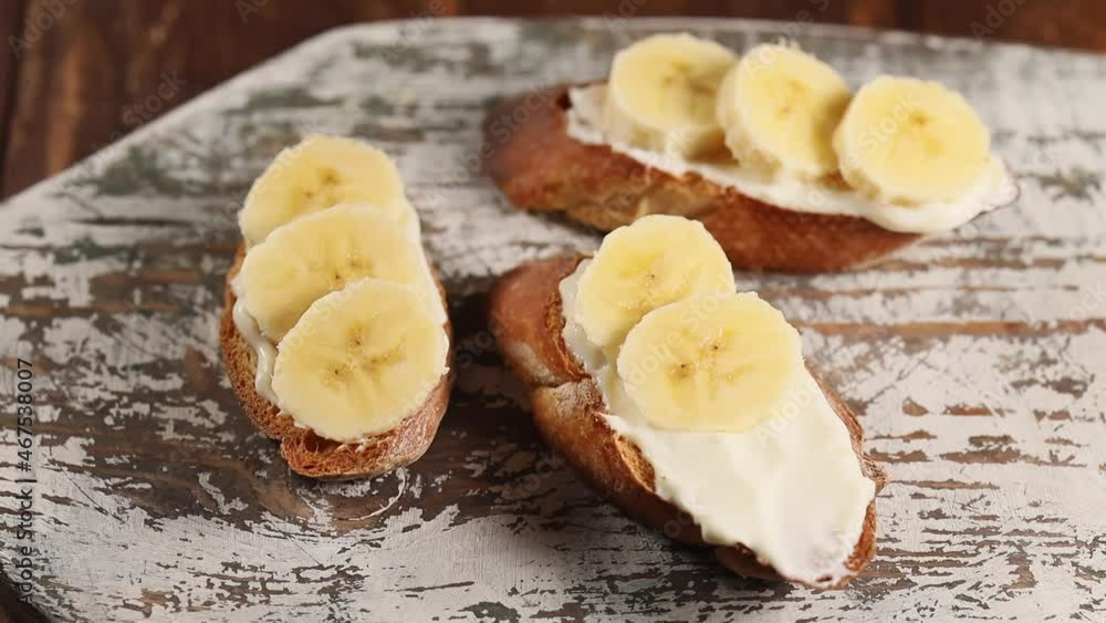 Preparing fruit breakfast, woman hand puts banana slice on cream cheese sandwich, close up Preparing fruit breakfast, woman hand puts banana slice on cream cheese sandwich, close up